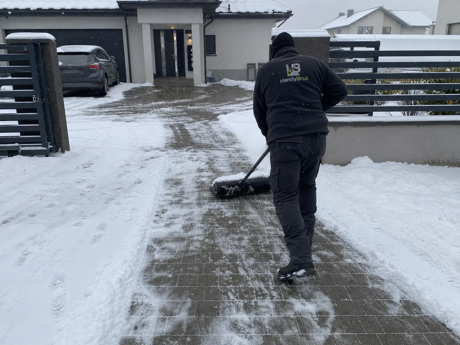 Pracownik HandyBruk odśnieża podjazd szeroką łopatą