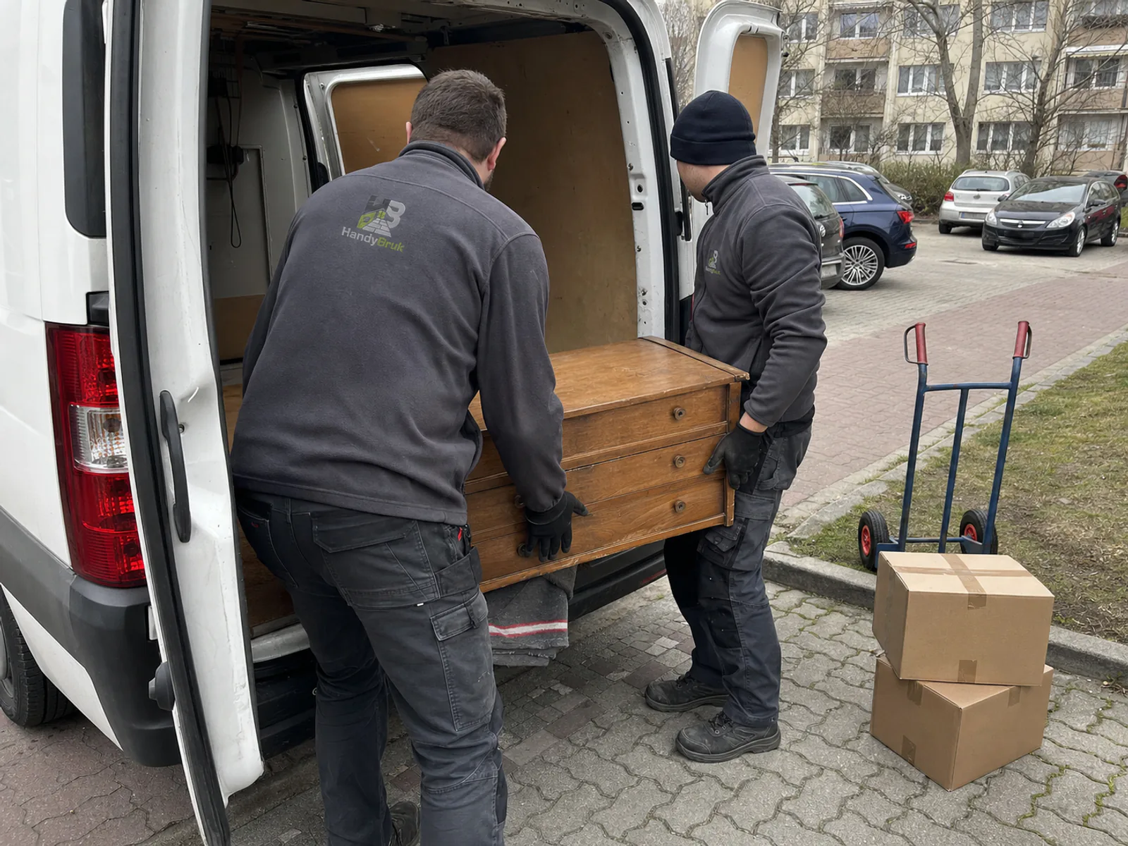 Dwóch pracowników HandyBruk ładuje drewnianą komodę do busa